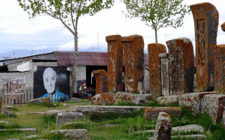 Noraduz. Un portrait de Charles Aznavour est accroché au mur face à l'entrée du champ de katchkars., mai 2023